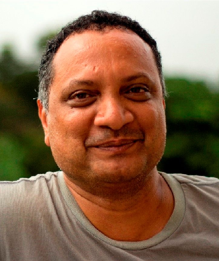 Portrait of Dr. Praveen Karanth, photographed outdoors against soft green foliage.